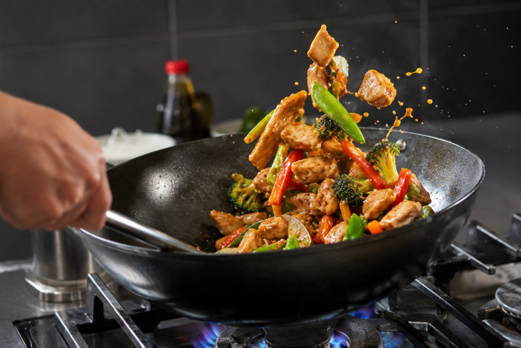 Close-up of chicken and vegetables being stir-fried in a hot pan for a healthy homemade meal.