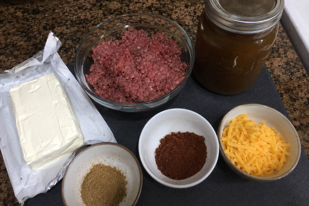 Ingredients for cheesy low-carb taco soup arranged on a dark cutting board.