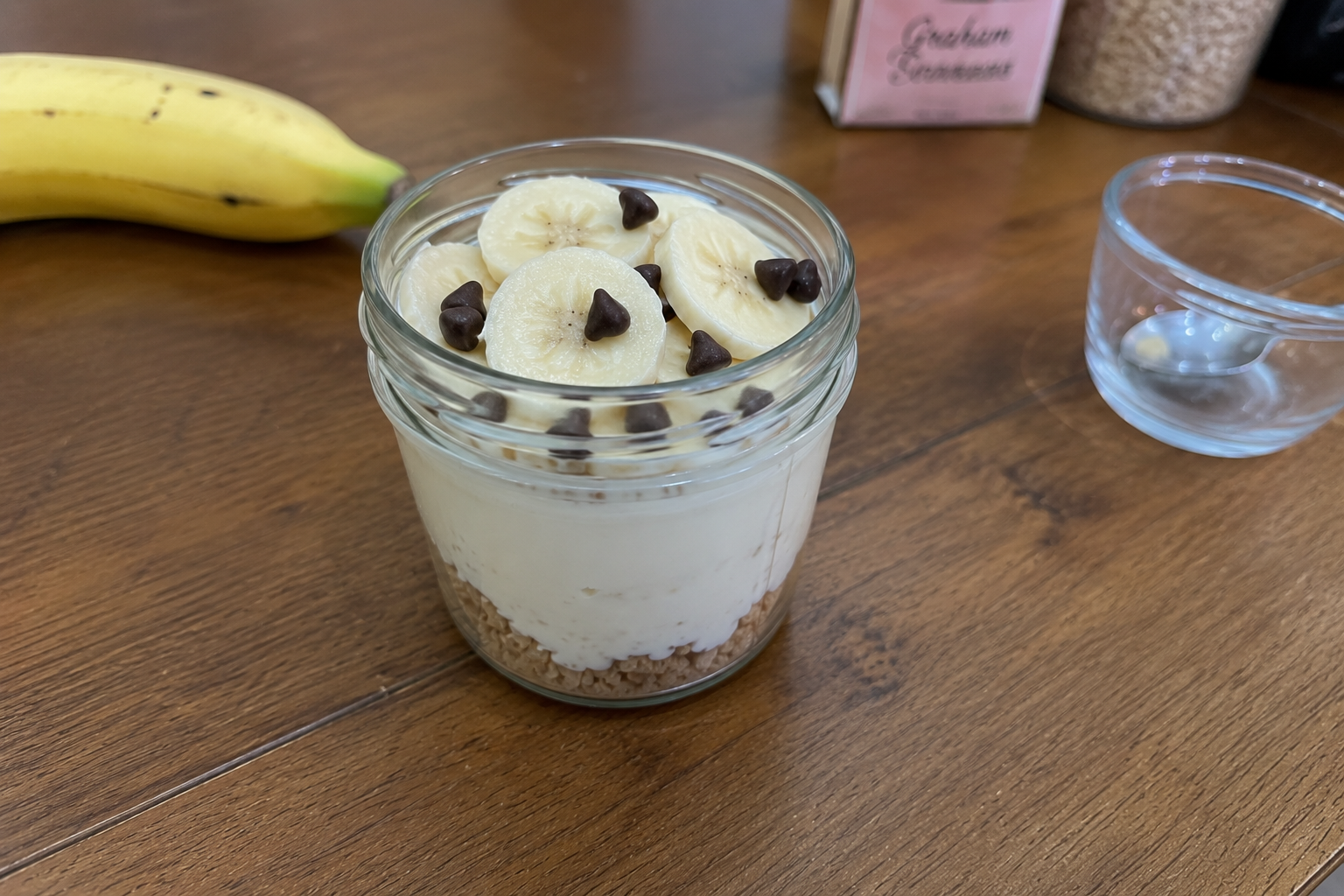 Layered no-sugar banana pudding breakfast cup with chocolate chips in sunlight
