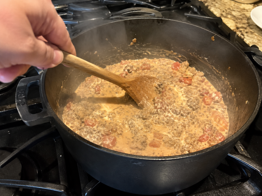 Stirring melted cream cheese and ground beef in a pot for keto soup